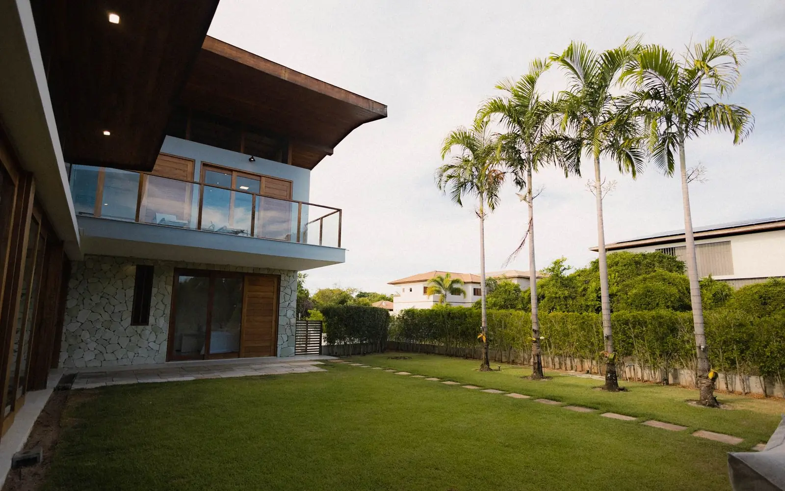 A tropical home with palms and a warmly lit modern home at dusk